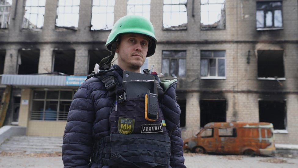 Oleksiy Savkevich standing in front of a burnt out school