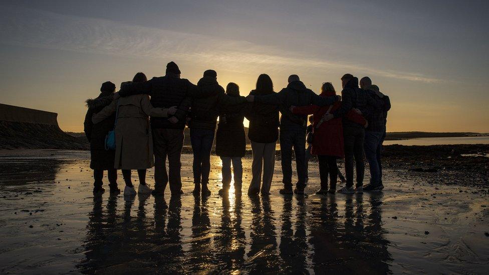 Members of the Wave Trauma Centre stand arm-in-arm as they watch the sun rise on Killough beach in County Down