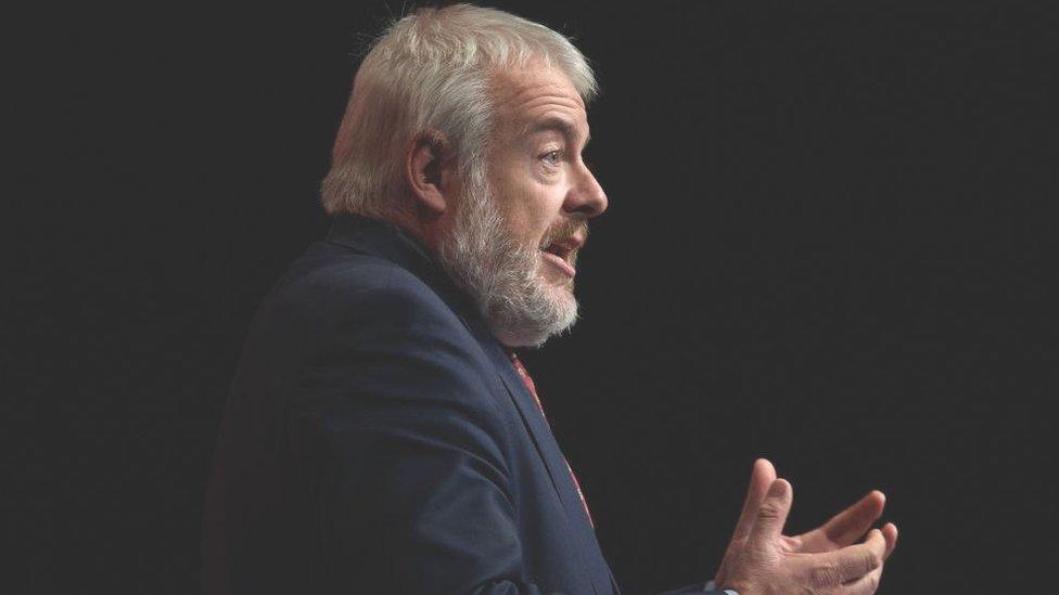 Carwyn Jones at the Labour party conference, pictured side on with his hands in a sort of cupping motion against a black background