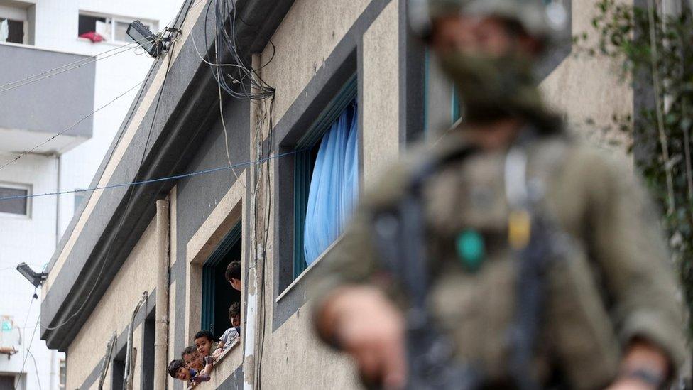 Palestinian children look out of a window as an Israeli soldier operates at Al-Shifa Hospital compound in Gaza City (22 November 2023)