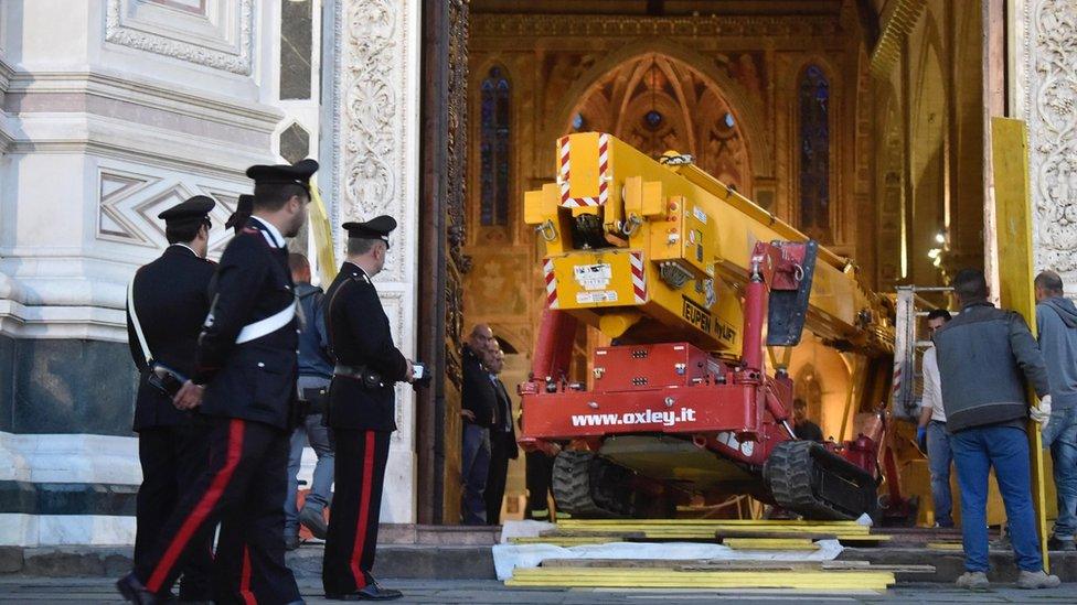 crane entering a church as police officers look on