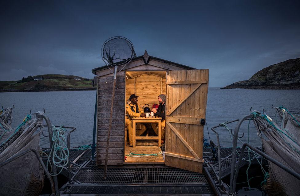 Portrait of Daniel and another man talking in a hut next to a lake