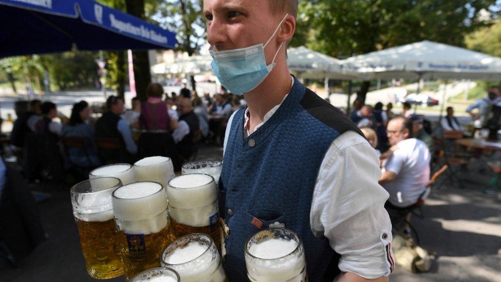 A server wearing a face mask carries mugs during a barrel tapping at a beer garden near Theresienwiese in Munich, September 2020