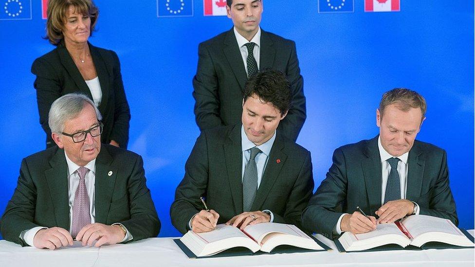 President of the European Commission Jean-Claude Juncker looks on as Canada's Prime Minister Justin Trudeau (C) and European Council President Donald Tusk sign the Comprehensive Economic and Trade Agreement