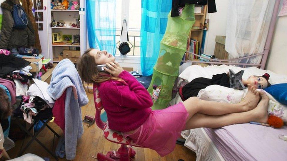 A woman sitting on her phone in a messy room.