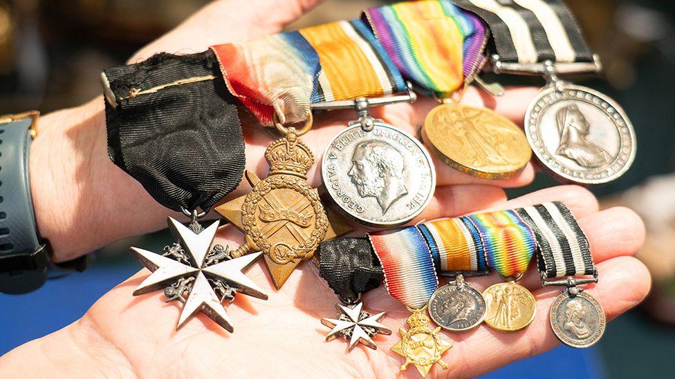 A person holding five medals with multi-coloured ribbons alongside five matching miniature dress medals.