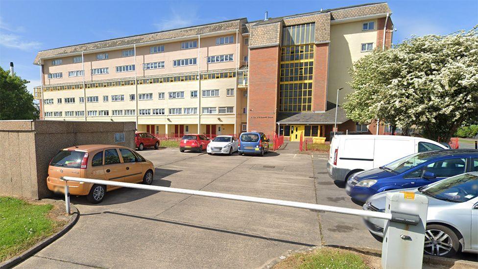 Rossett House which has pink cladding and yellow doors and window frames with a car park protected by a barrier at the front