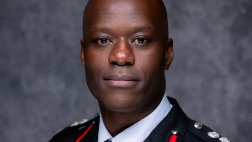 Wayne Brown's head and shoulders are pictured. He is wearing his fire service uniform in front of a grey background and is looking at the camera.