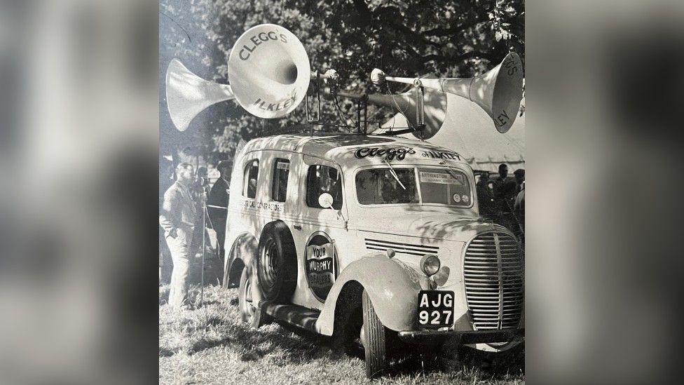 A black and white photo of a van from the 1940s with speakers on the top 