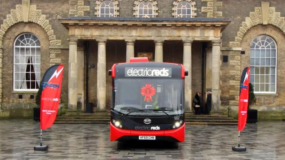 A red single decker bus with 'electric reds' in the destination display