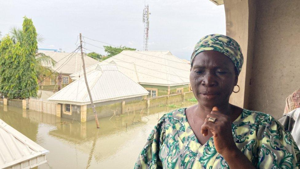 A woman, Mrs Lamine Y Ibrahim, stands on a balcony above floodwaters.