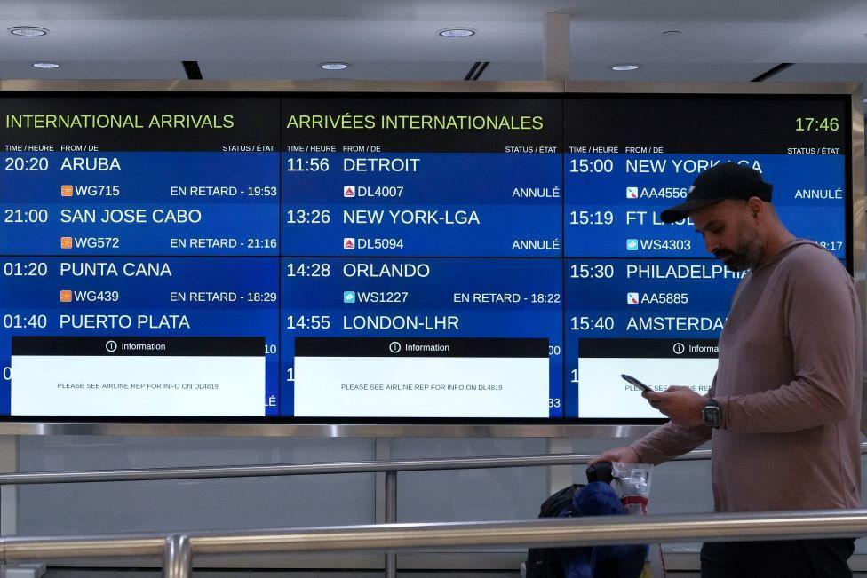 A passenger walks past airport timetables saying 'Delays' next to sceduled flights.