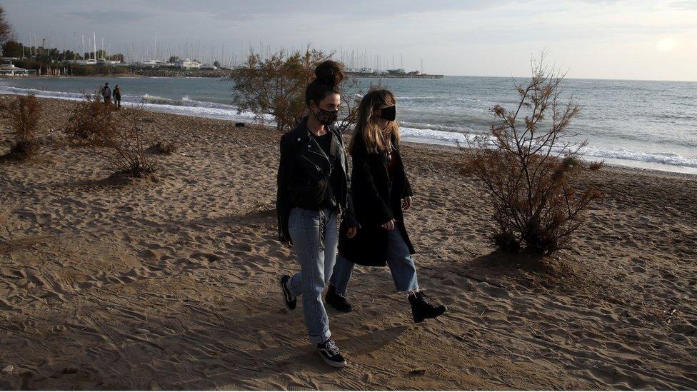 People wearing protective face masks walk on a beach during an unusual warm day in Athens