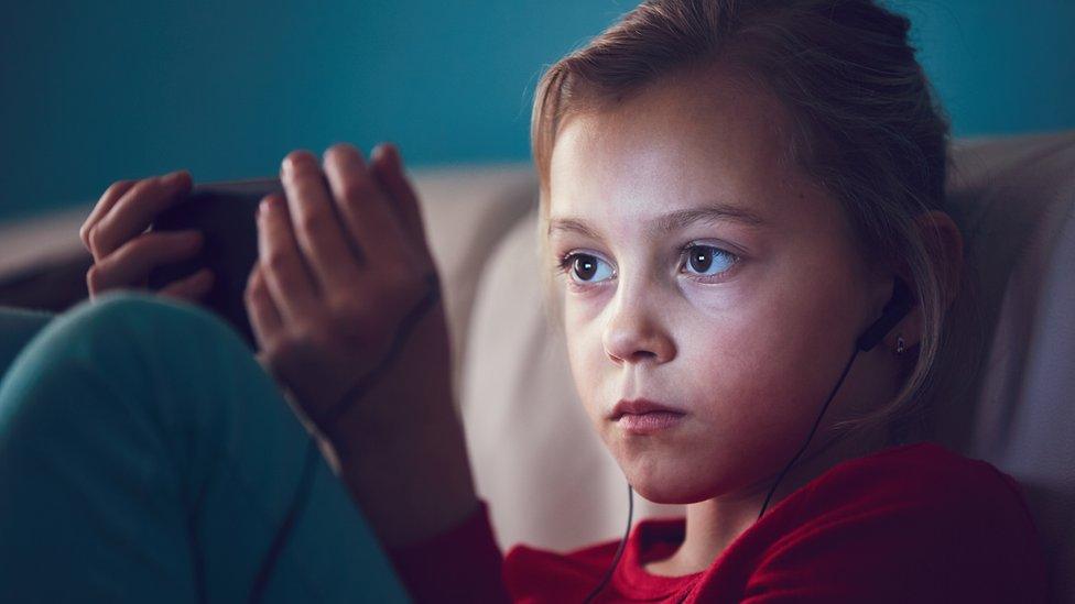 Child wearing headphones watching something on a smartphone.