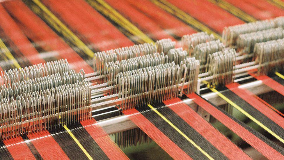 A textile loom in operation with a range of red, black and yellow threads