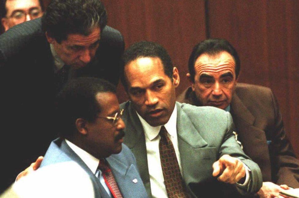 Johnnie Cochran, OJ Simpson and Robert Shapiro sitting in court with Robert Kardashian leaning over them