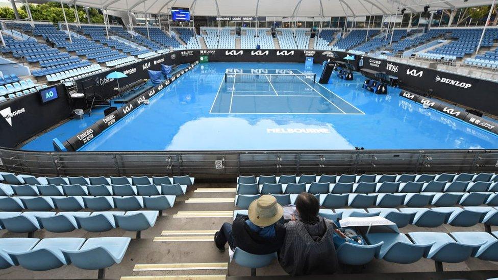 two spectators look on at a flooded tennis court, as wet weather delays play at the Australian Open in Melbourne .