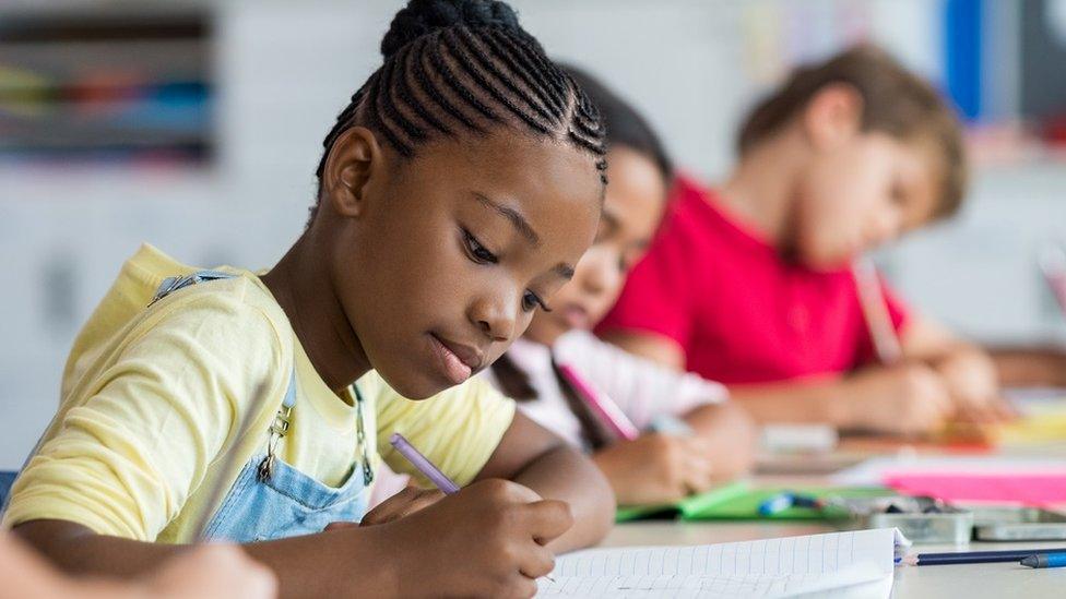 Girl at a desk in her classroom, writing notes on her notebook during a lesson.