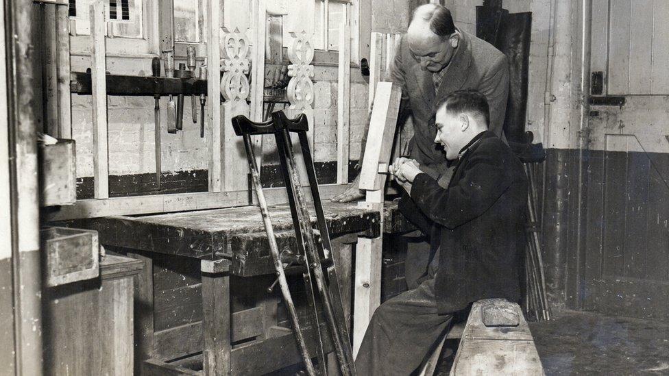 A man with a crutch at his work station with a man watching 1930s