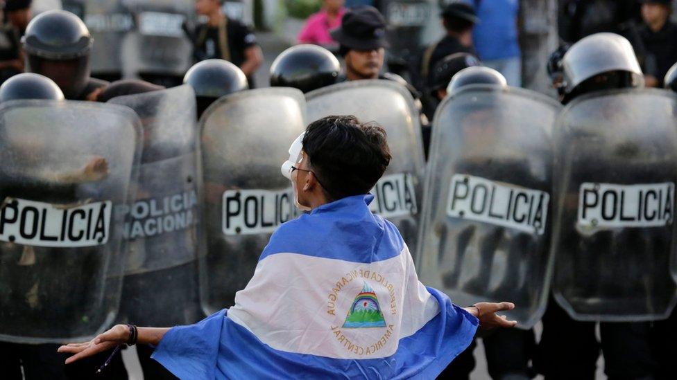 A masked youngster protests against Nicaraguan President Daniel Ortega's government in front of a line of riot police blocking a street in Managua, on September 13, 2018