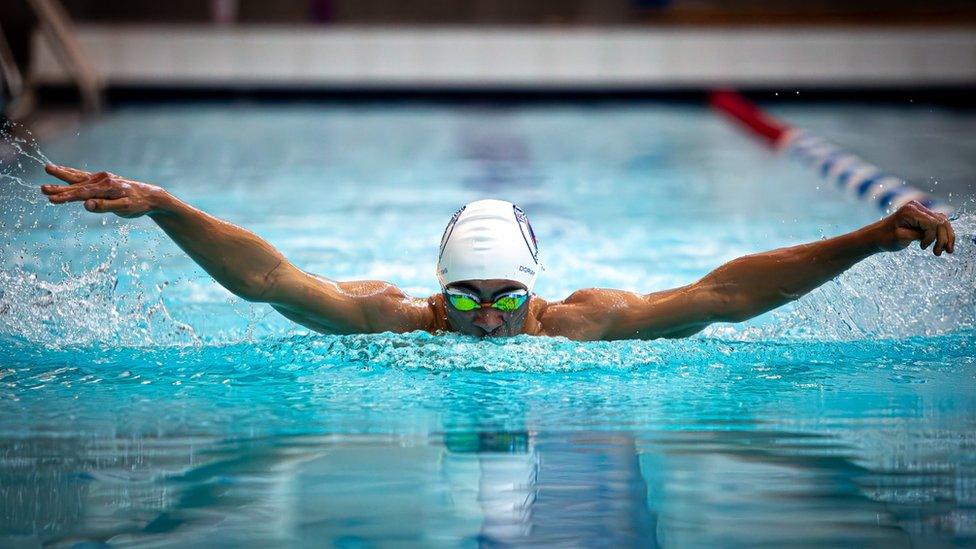 A man in a pool swimming wearing a white swim cap