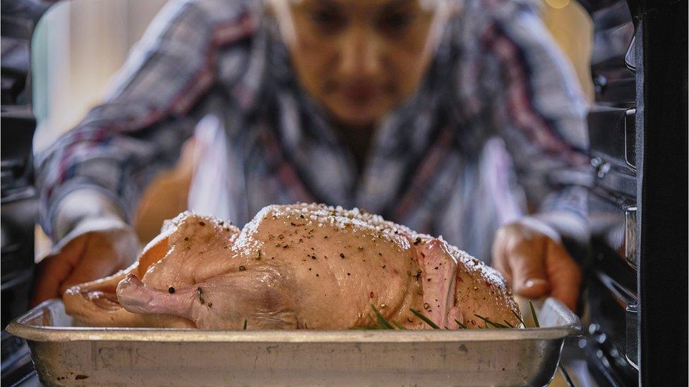 Person putting a chicken in an oven