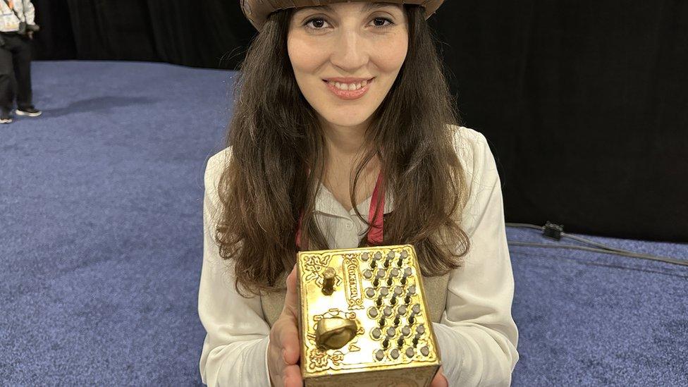 A woman holding the Ohm's Quest - a metal box covered in switches and buttons, so it can function as a game