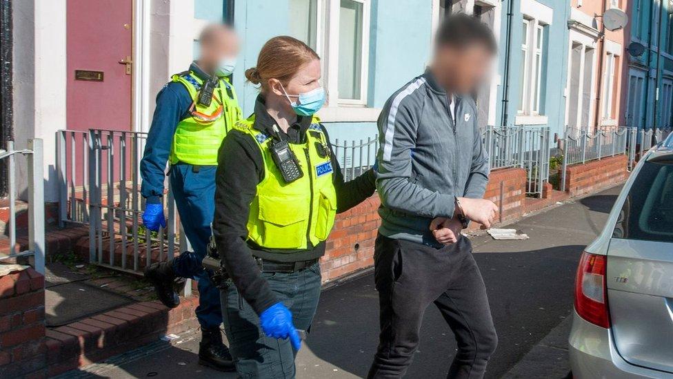 Police officer leads man in handcuffs out of a house