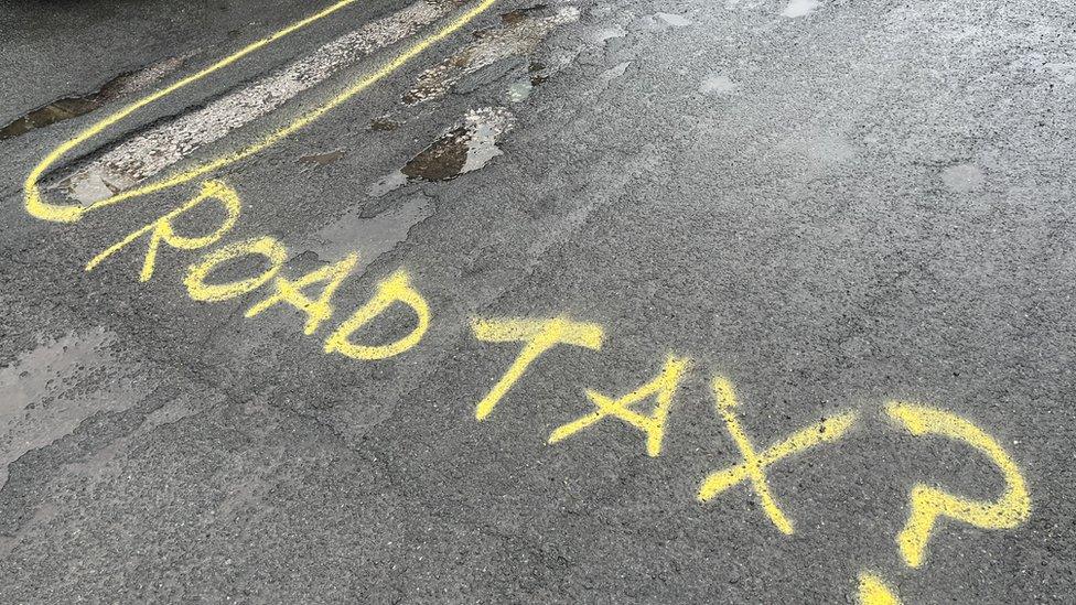 Graffiti next to potholes on the road