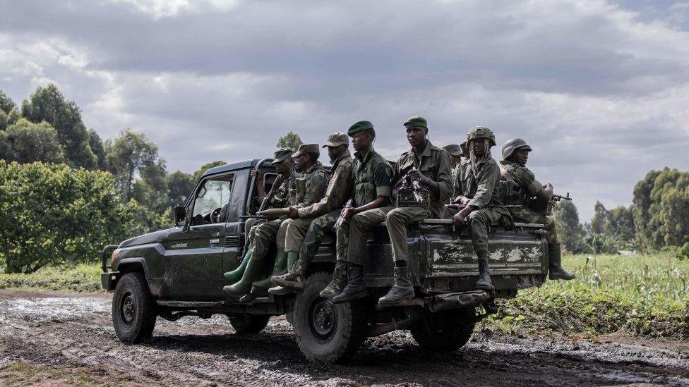 Armed M23 fighters sit on the back of a pickup truck