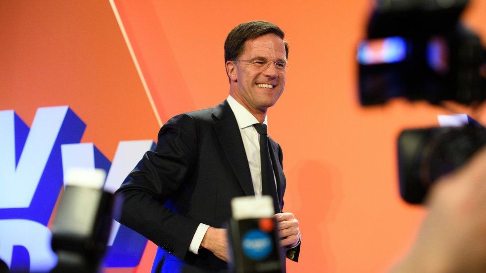 Centre-right leader Mark Rutte smiling on a stage in front of orange backdrop