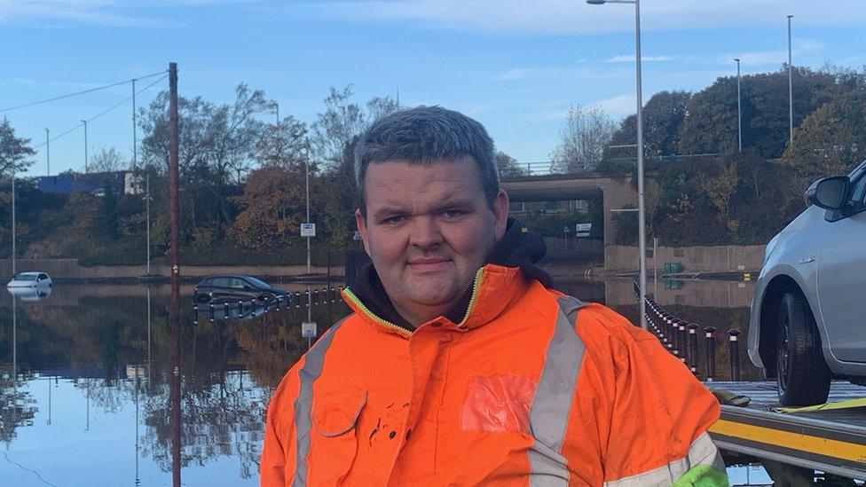 A man stands in front of cars submerged in food water in a town