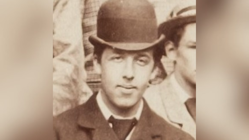 A black and white archive image of Oscar Wilde as a student. He is wearing a black bowler hat and suit.