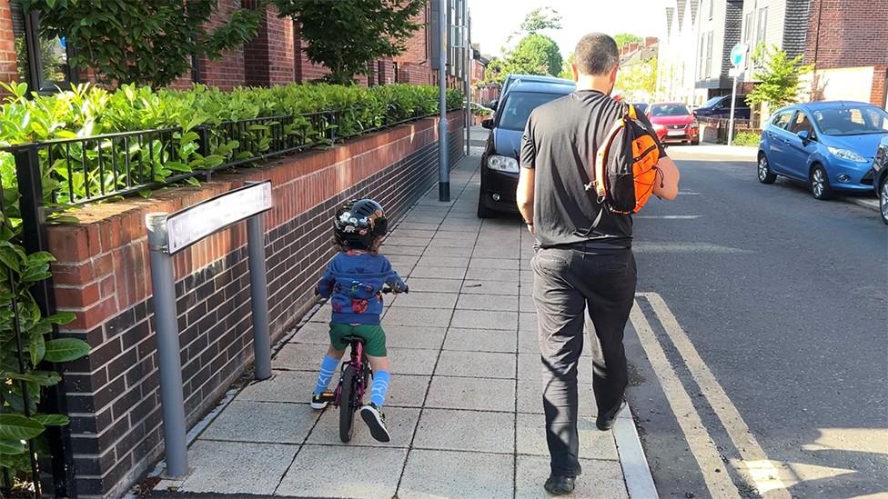 Child on bike with man walking on pavement blocked by parked car