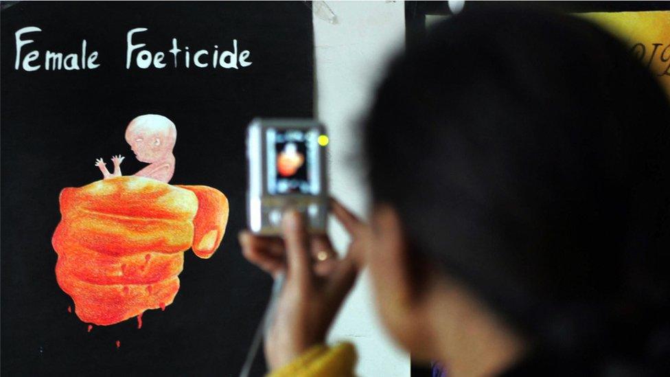 A young girl, Aman Kaur takes a photograph of paintings displayed during the opening of the art exhibition 'Female Foeticide' at Virsa Vihar hall in Amritsar on January 25, 2009