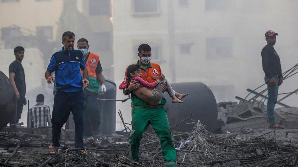 A Palestinian man carries a wounded girl after recovering her from the rubble of a destroyed area following Israeli air strikes in Gaza City, 25 October 2023.