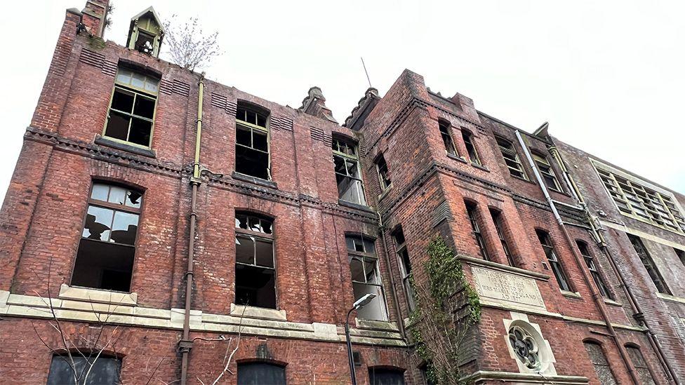 St Joseph's orphanage, a large red brick building with many windows missing and broken and plants growing up the front