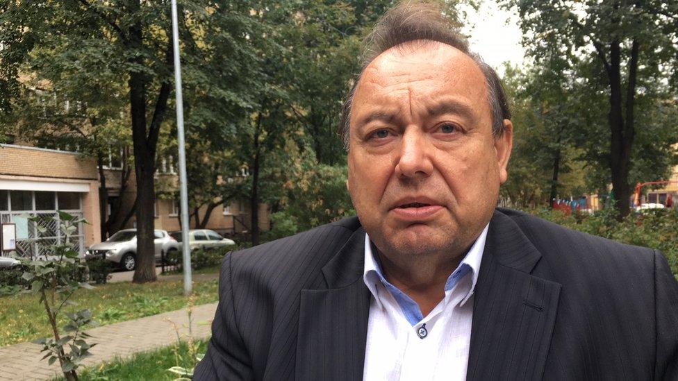 Gennady Gudkov is pictured wearing an open-collared shirt and suit jacket in a quiet, leafy street