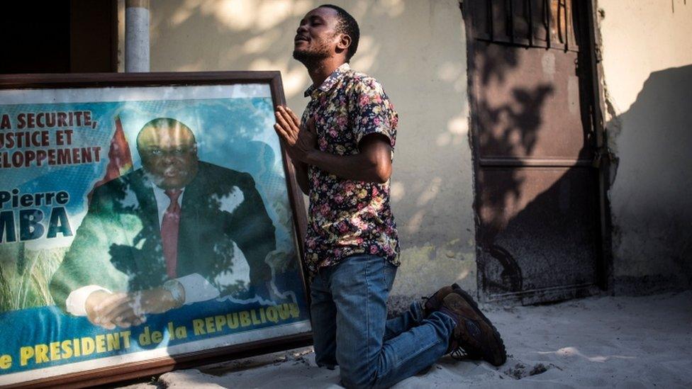 A supporter of Jean-Pierre Bemba prays as he kneels next to his picture at the Congolese Liberation Movement (MLC) headquarter in Kinshasa on June 8, 2018