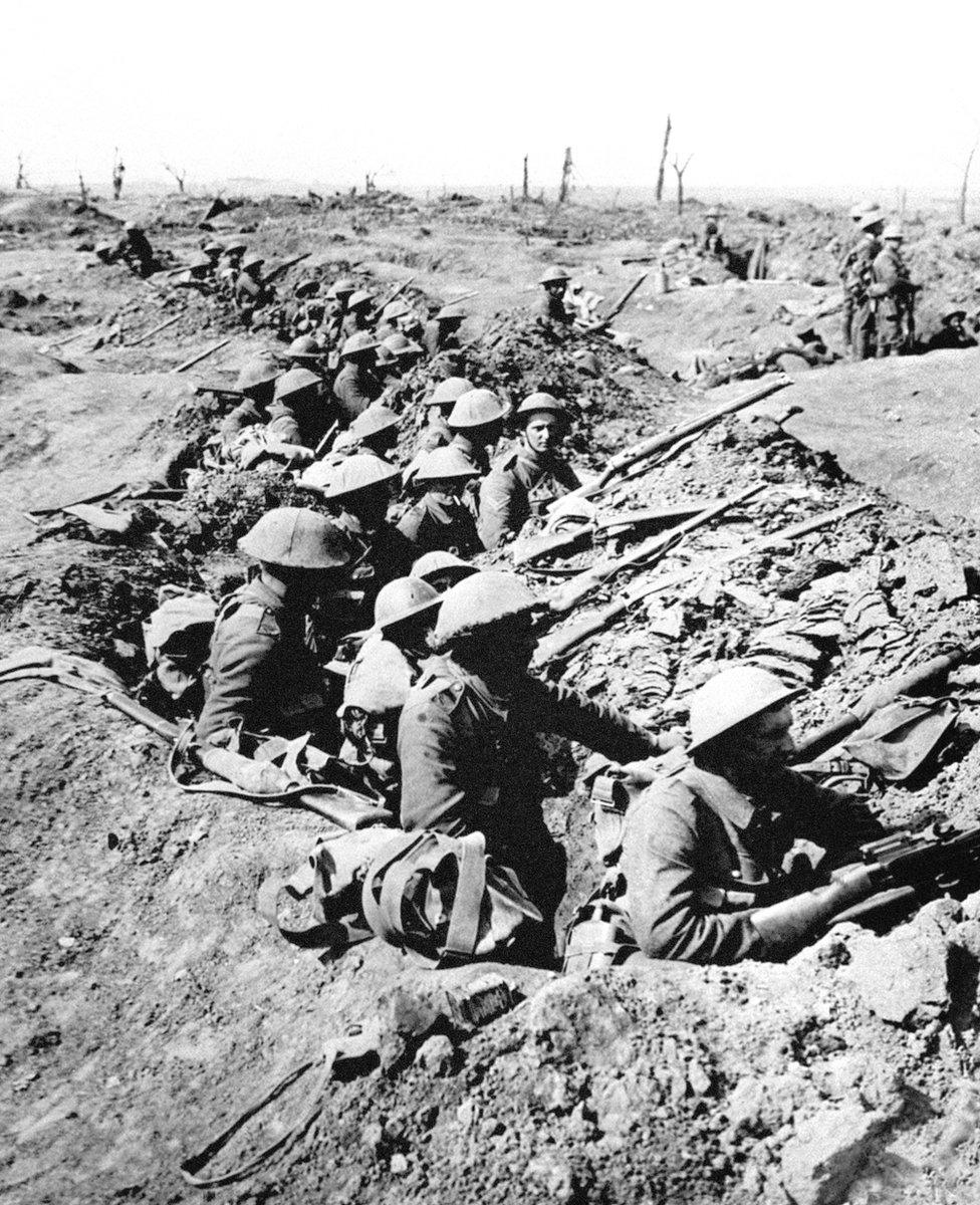 British infantrymen occupy a shallow trench in a ruined landscape before an advance during the Battle of the Somme