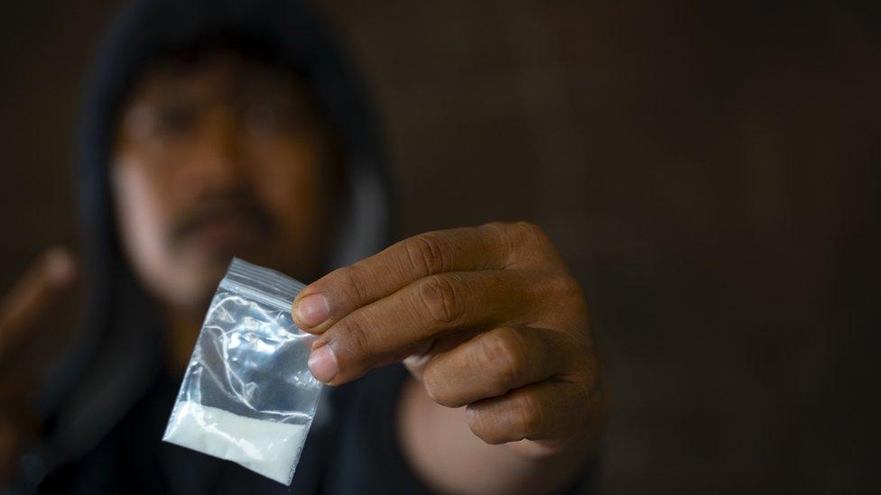 man hoodie with blurred face holding a plastic bag with while powder