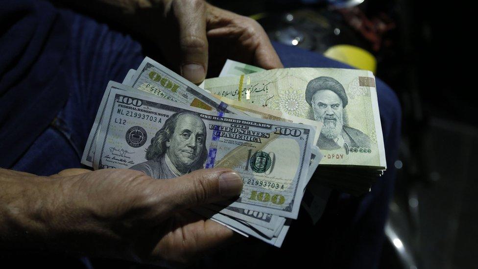 A man holds US dollars and Iranian rials at an exchange shop in Tehran, Iran (8 August 2018)