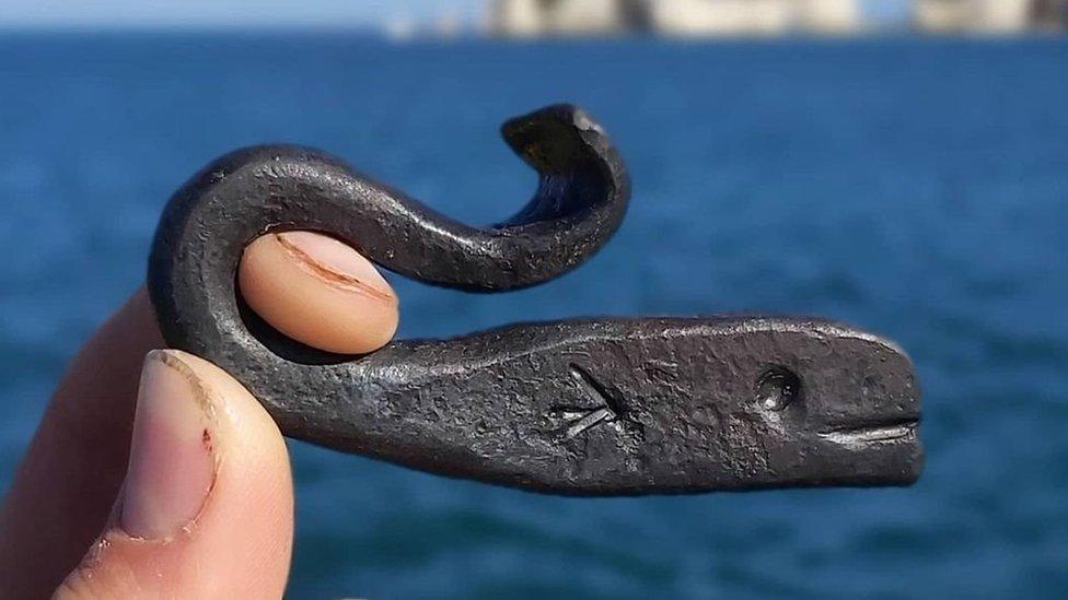 A close-up of a bottle opener shaped like a whale, held against a background of the ocean