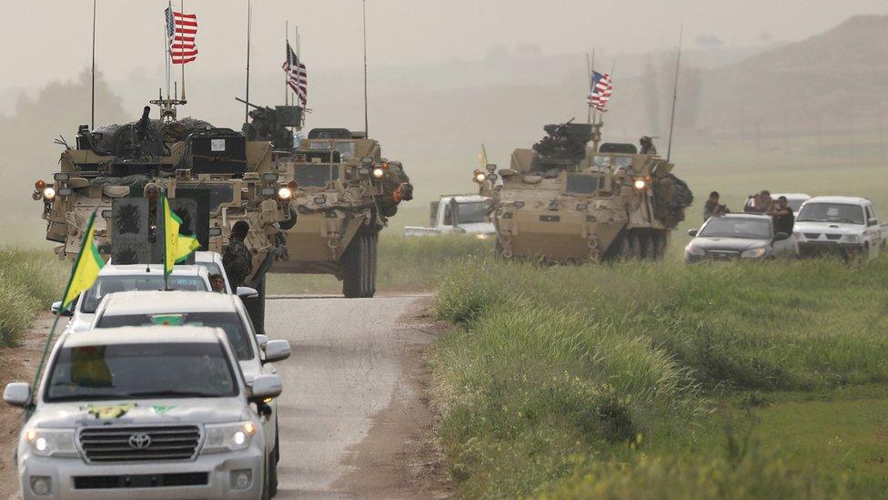 Kurdish fighters from the People's Protection Units (YPG) drive in front of US military armoured vehicles in northern Syria (28 April 2017)