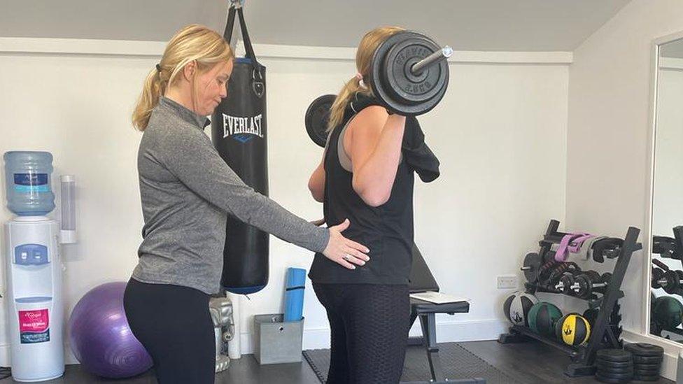 Kim Ovel with one of her personal training clients, assisting her with a squat