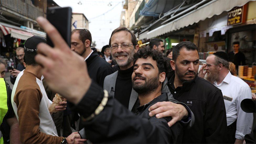 Zehut party leader Moshe Feiglin (C) poses for a selfie with a man at a market in Jerusalem on 4 April 2019