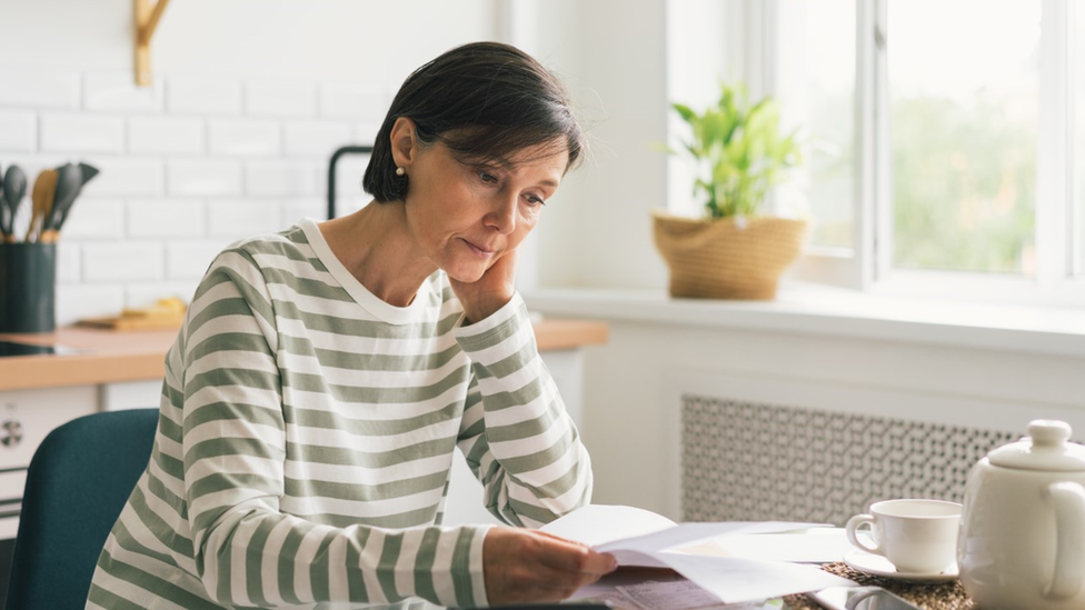 Woman reads energy bill at kitchen table