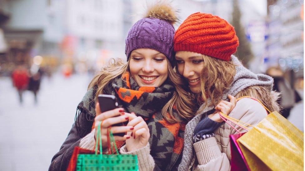 Two women looking at a phone while Christmas shopping