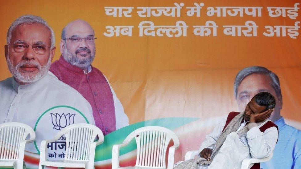 A worker of Bharatiya Janata Party (BJP) takes a nap in front of the party"s campaign billboard featuring Prime Minister Narendra Modi (L) and the BJP"s president Amit Shah at a party office in New Delhi in this February 10, 2015 file photo.