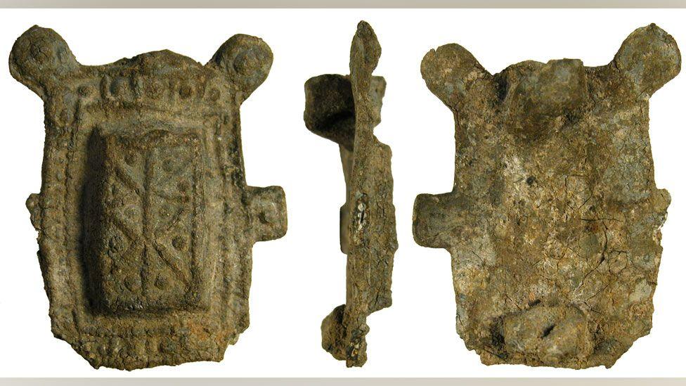 Three views of a rectangular lead brooch. On the left is its front, which has a raised centre and a pattern made up of dots struck into the metal. In the middle is a side view. On the right is the back view. It has lost its pin.